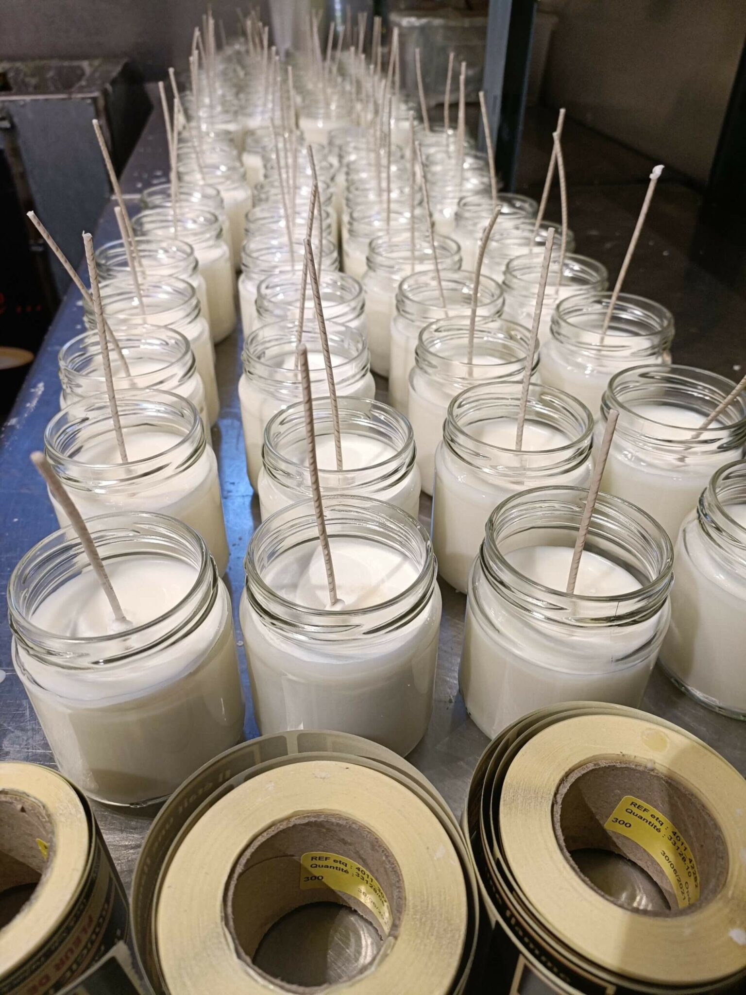 Photo de bougies artisanales en phase de séchage, avec des mèches en coton à ajuster.